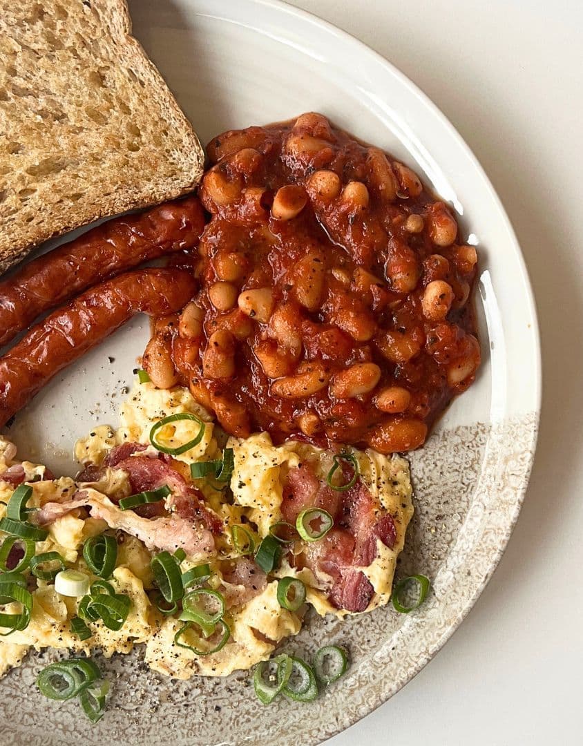 Klasyczne śniadanie z puszystą jajecznicą, świeżymi warzywami, fasolką i frankfurterkami oraz pieczywem, podane na eleganckim talerzu